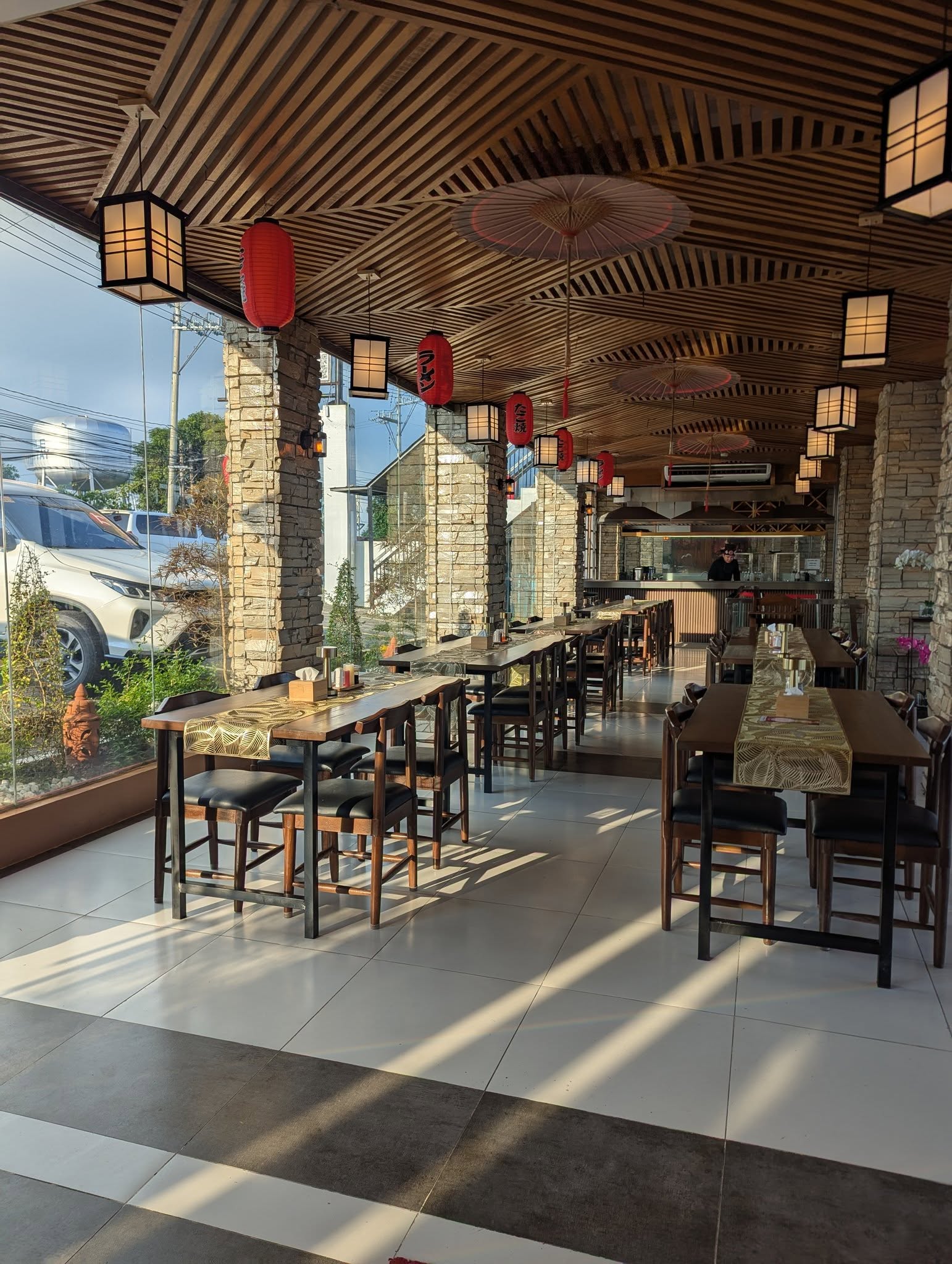Wide shot of a minimalist, light-filled cafe interior with wooden tables, archways, and a barista behind a curved counter